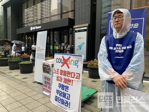 ▲20일, 뒷편으로 쿠팡 본사 직원들이 보이는 가운데, 쿠팡 택배 노동자가 현수막을 들고 있다.